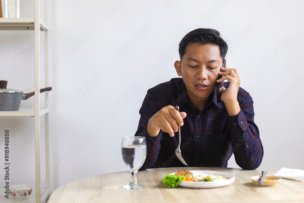 Asian Man Wear Casual Eating Chicken Steak While Answer The Call At Home Asian Man Wear Casual Eating Chicken Steak While Answer The Call At Home