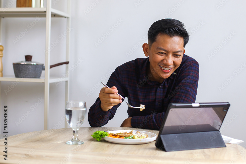 Happy Asian Man With Braces Enjoying Eat Chicken Steak While Looking At Digital Tablet At Home Happy Asian Man With Braces Enjoying Eat Chicken Steak While Looking At Digital Tablet At Home