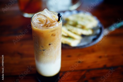 a glass of palm sugar milk coffee, with several ice cubes visible on the surface