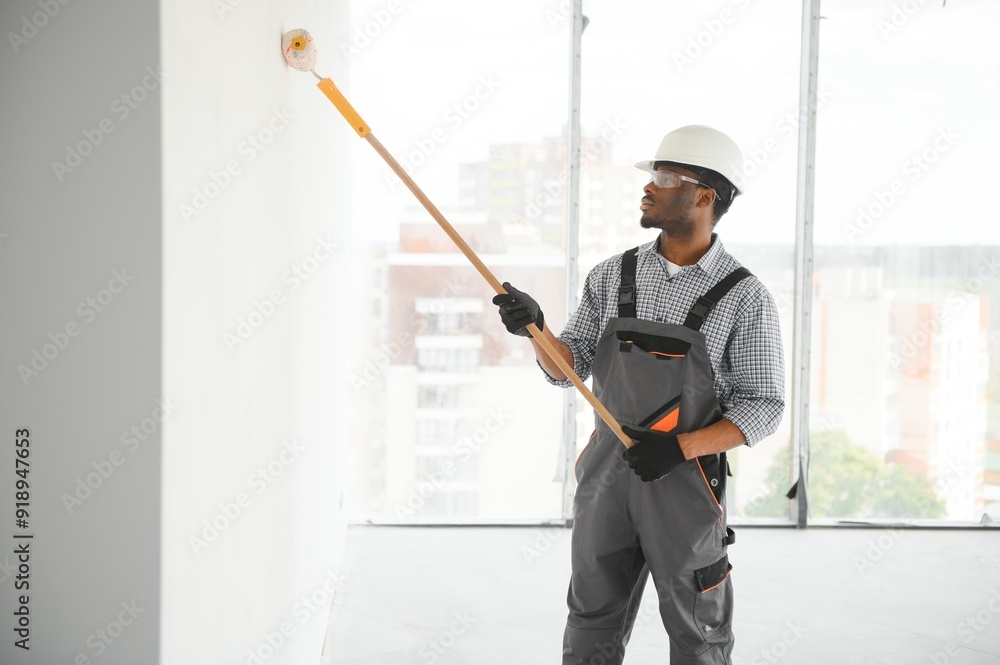 African man paints a white wall with a roller. Repair of the interior African man paints a white wall with a roller. Repair of the interior