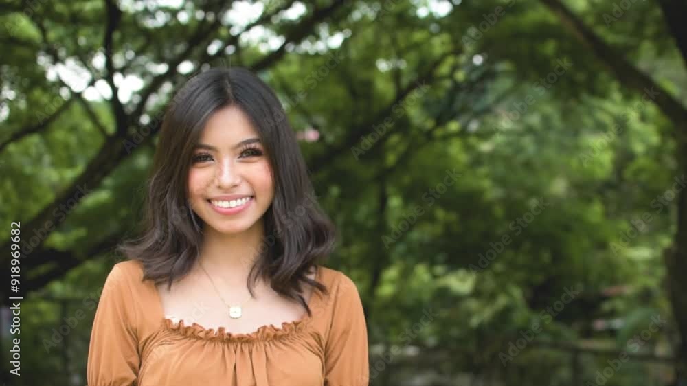 A happy young asian woman feeling elated, smiling ear to ear. Outdoor park scene. Copy space on the right. A happy young asian woman feeling elated, smiling ear to ear. Outdoor park scene. Copy space on the right.