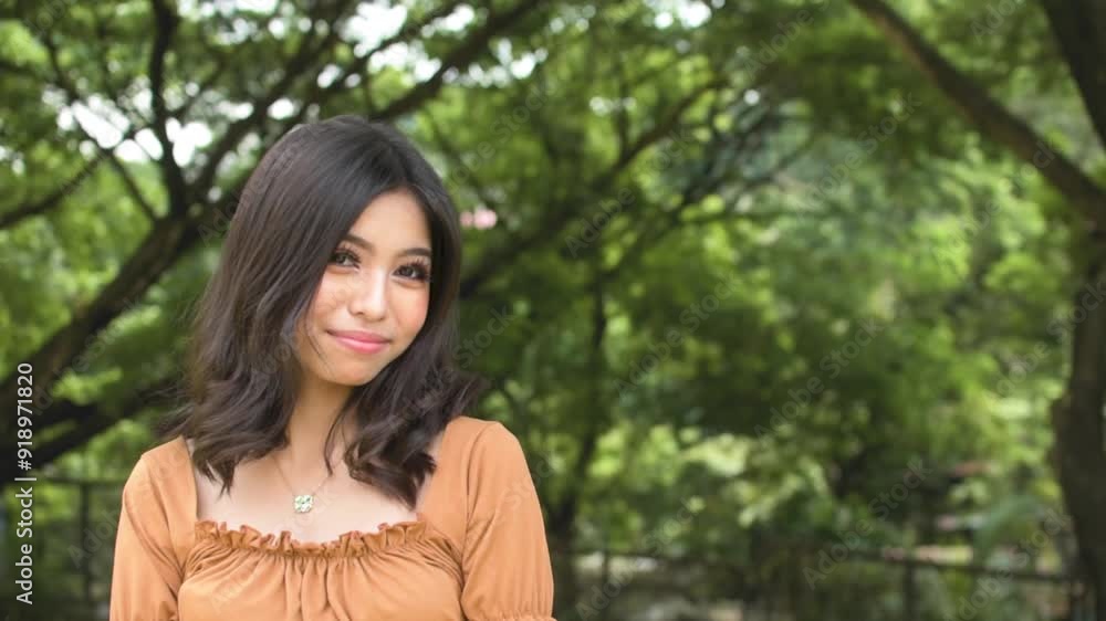 A young teenage asian woman trying to look cute for someone, smiling trying to get attention. Outdoor park scene. Copy space on the right. Slowed down 50 percent. A young teenage asian woman trying to look cute for someone, smiling trying to get attention. Outdoor park scene. Copy space on the right. Slowed down 50 percent.