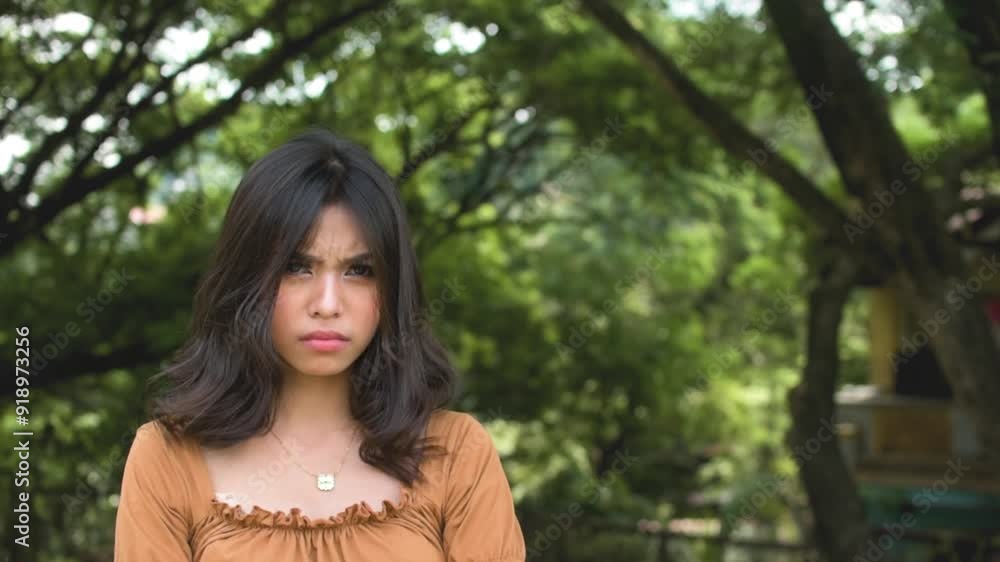 A young teenage asian woman looks annoyed and upset, refusing to budge. Outdoor park scene. Copy space on the right. Slowed down 50 percent. A young teenage asian woman looks annoyed and upset, refusing to budge. Outdoor park scene. Copy space on the right. Slowed down 50 percent.