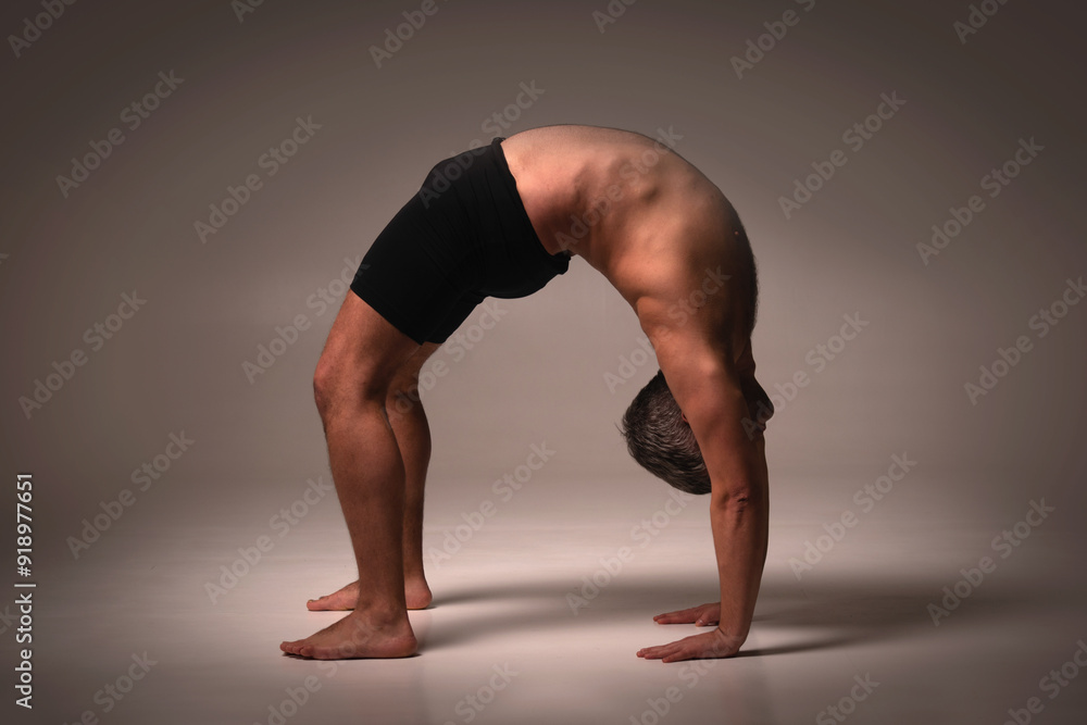 Urdhva Dhanurasana (Wheel Pose), Ashtanga yoga Side view of man wearing sportswear doing Yoga exercise against dark background. Urdhva Dhanurasana (Wheel Pose), Ashtanga yoga Side view of man wearing sportswear doing Yoga exercise against dark background.