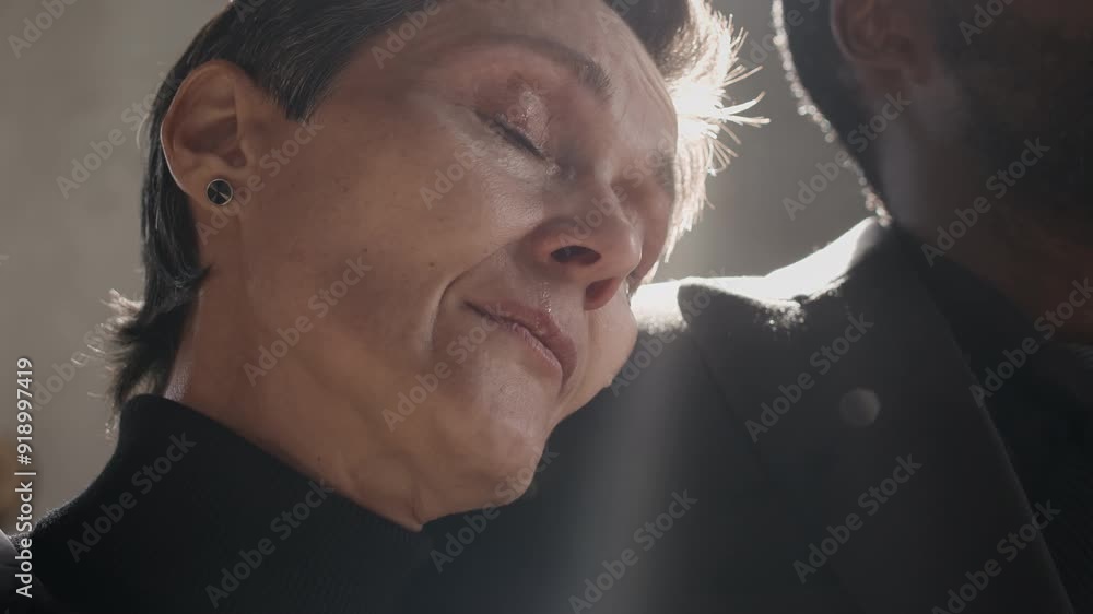 Close up view of Caucasian adult woman crying on shoulder of her African American friend and wiping her mouth at funeral ceremony Close up view of Caucasian adult woman crying on shoulder of her African American friend and wiping her mouth at funeral ceremony