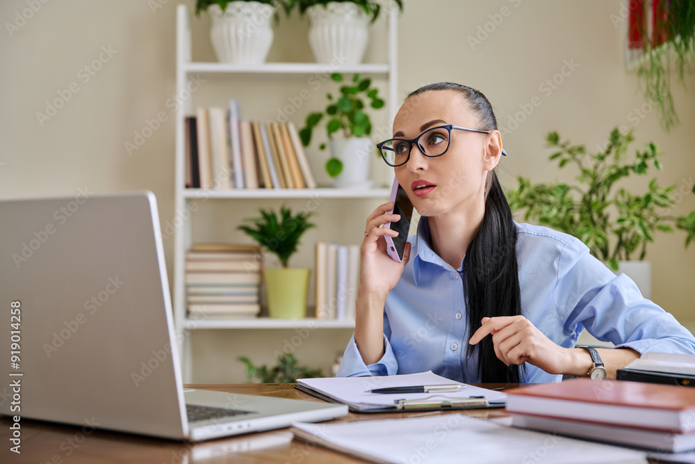 Business woman talking on mobile phone sitting at desk with computer Business woman talking on mobile phone sitting at desk with computer