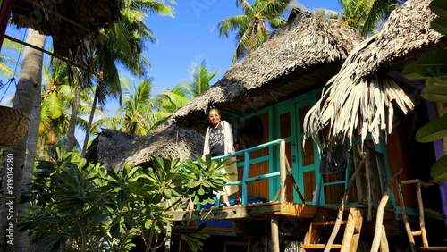 lächelnde Asiatin steht auf Balkon eines  Ferienhauses unter Palmen auf der Insel Timor in Indonesien