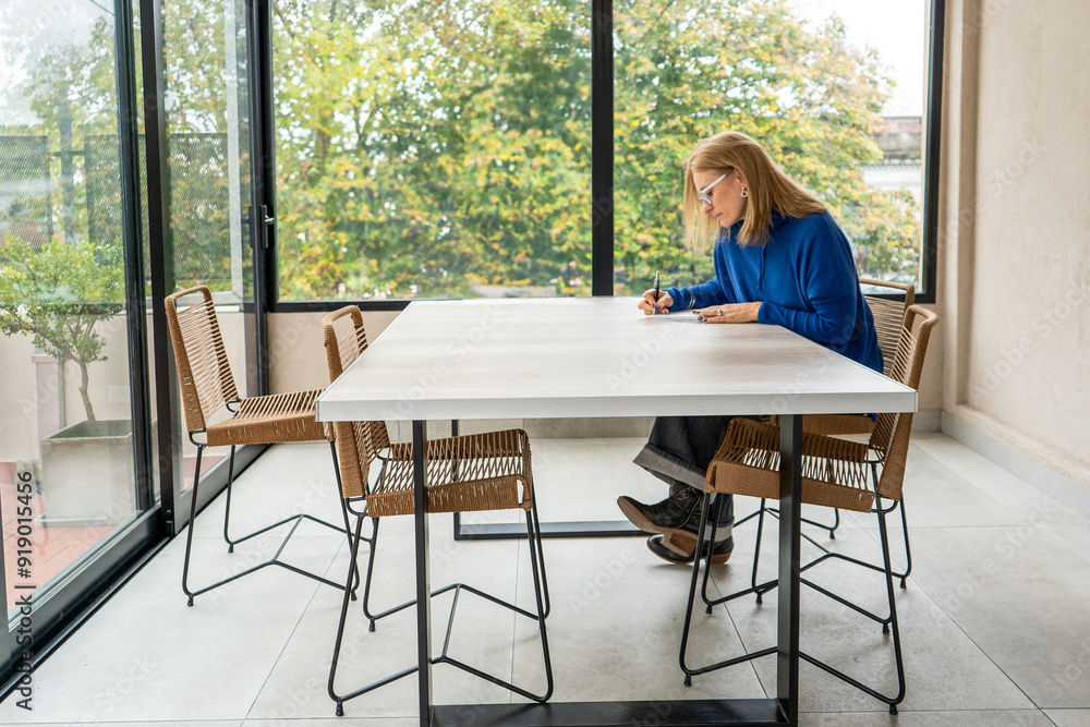 Mid-adult woman writing at a modern outdoor table Mid-adult woman writing at a modern outdoor table