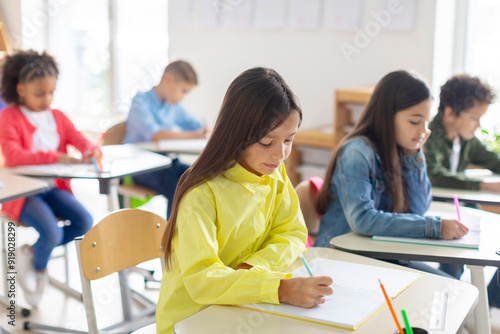 Junior school children writing in their copybooks, having exam, creating studious atmosphere in classroom interior