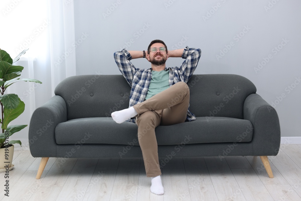 Smiling man with hands behind his head relaxing on sofa at home Smiling man with hands behind his head relaxing on sofa at home