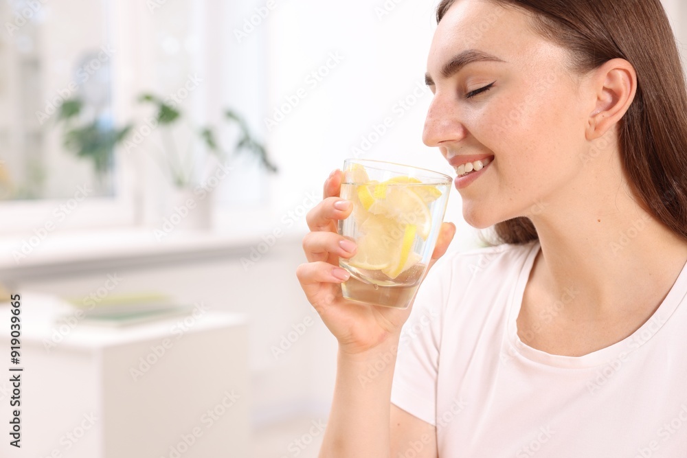 Woman drinking water with lemon indoors. Space for text Woman drinking water with lemon indoors. Space for text