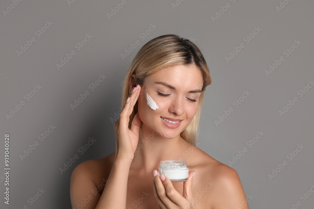 Beautiful woman with cream on her face against grey background Beautiful woman with cream on her face against grey background