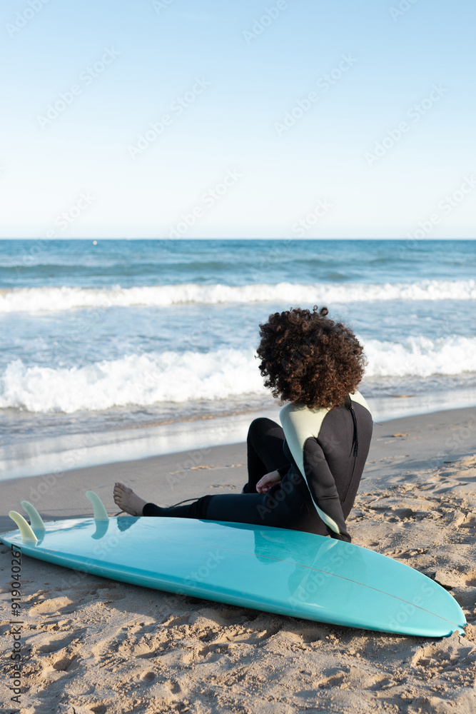 Obraz premium Woman in wetsuit with surfboard lying on sandy beach