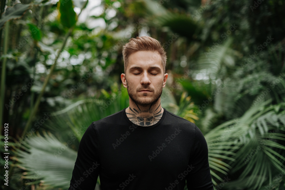 Handsome man with tattoo standing in botanical garden, in the middle of lush green foliage, looking at camera. Handsome man with tattoo standing in botanical garden, in the middle of lush green foliage, looking at camera.