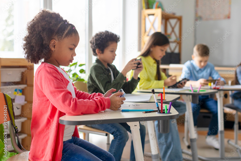Schoolkids having break during lessons and playing games on smartphones in classroom interior Schoolkids having break during lessons and playing games on smartphones in classroom interior