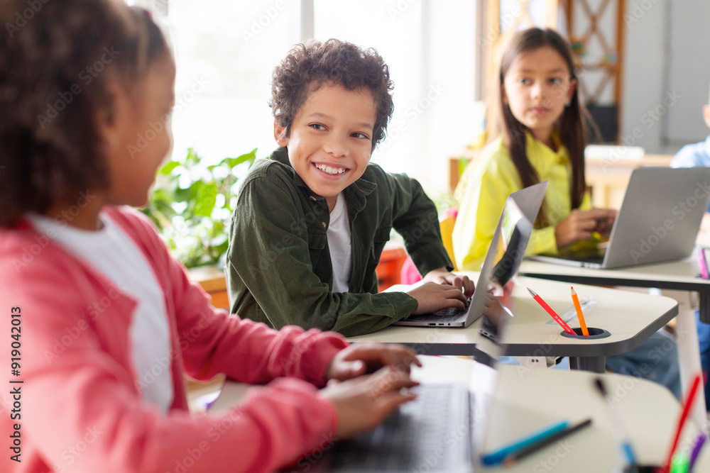 Latin schoolboy talking to girl while having tech lesson, children using laptops. Kid actively discussing and collaborating with friend Latin schoolboy talking to girl while having tech lesson, children using laptops. Kid actively discussing and collaborating with friend