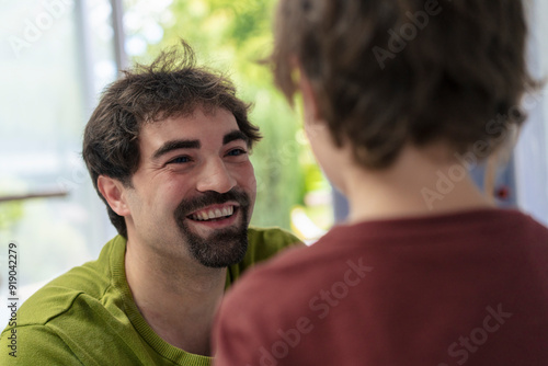 Happy father with goatee talking to son at home photo