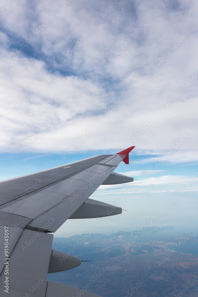 Obraz premium Airplane flying under cloudy sky over ocean and land