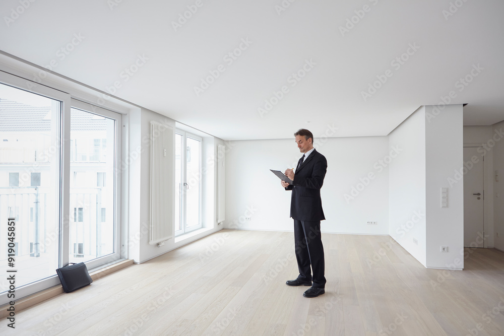 Businessman standing and holding file in empty apartment Businessman standing and holding file in empty apartment
