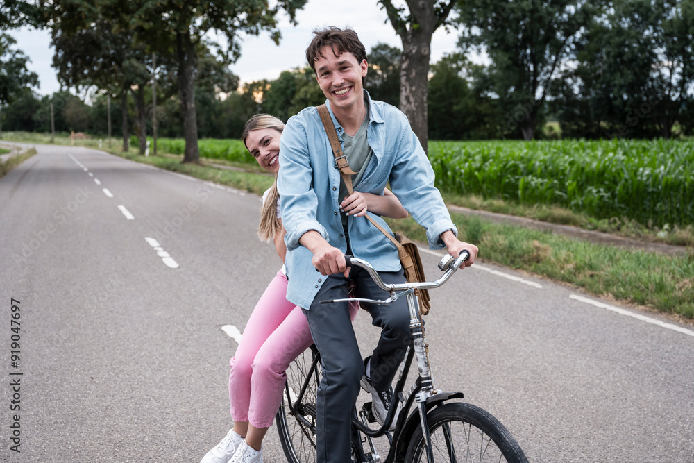 Happy woman sitting behind boyfriend riding bicycle on road Happy woman sitting behind boyfriend riding bicycle on road