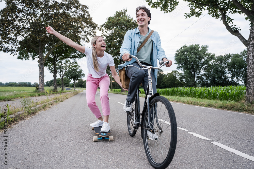 Carefree woman skateboarding with boyfriend riding bicycle on road Carefree woman skateboarding with boyfriend riding bicycle on road