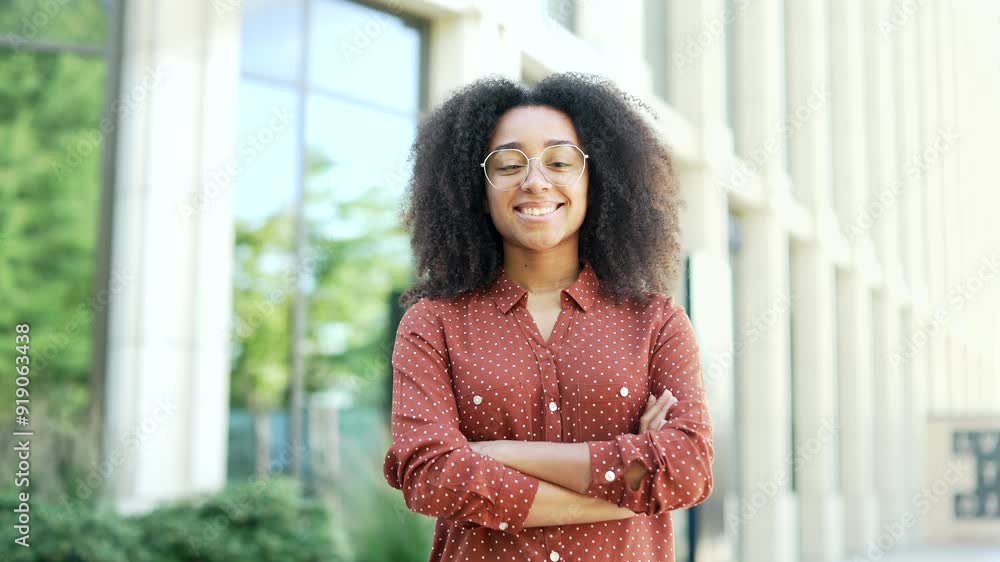 Portrait of smiling happy woman standing confidently outdoors in front of modern office building. Professional black woman with curly hair andglasses, symbolizing success, empowerment, and positivity Portrait of smiling happy woman standing confidently outdoors in front of modern office building. Professional black woman with curly hair andglasses, symbolizing success, empowerment, and positivity