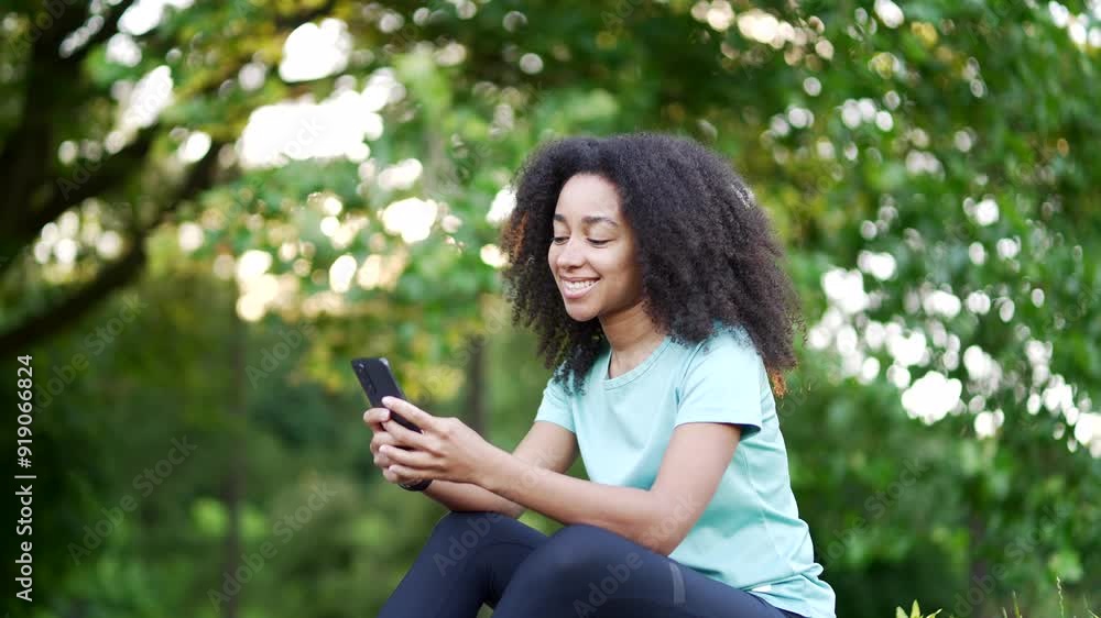 Young happy african american sportswoman using a phone while sitting in an urban city park. Smiling black woman athlete typing a message, chatting online, browsing web, watching, reading notifications Young happy african american sportswoman using a phone while sitting in an urban city park. Smiling black woman athlete typing a message, chatting online, browsing web, watching, reading notifications