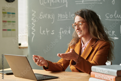 Side view portrait of smiling female teacher talking to video chat during online lesson with student and gesturing photo