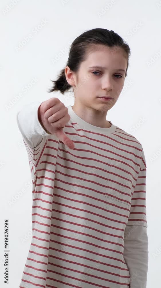 Stern Caucasian teenage boy showing thumbs down gesture in disagree or rejection, standing alone on white background. Vertical video. Stern Caucasian teenage boy showing thumbs down gesture in disagree or rejection, standing alone on white background. Vertical video.