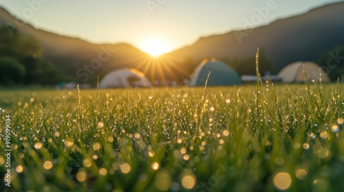 Dewdrops on Grass with Blurry Sunrise and Tents in Background photo