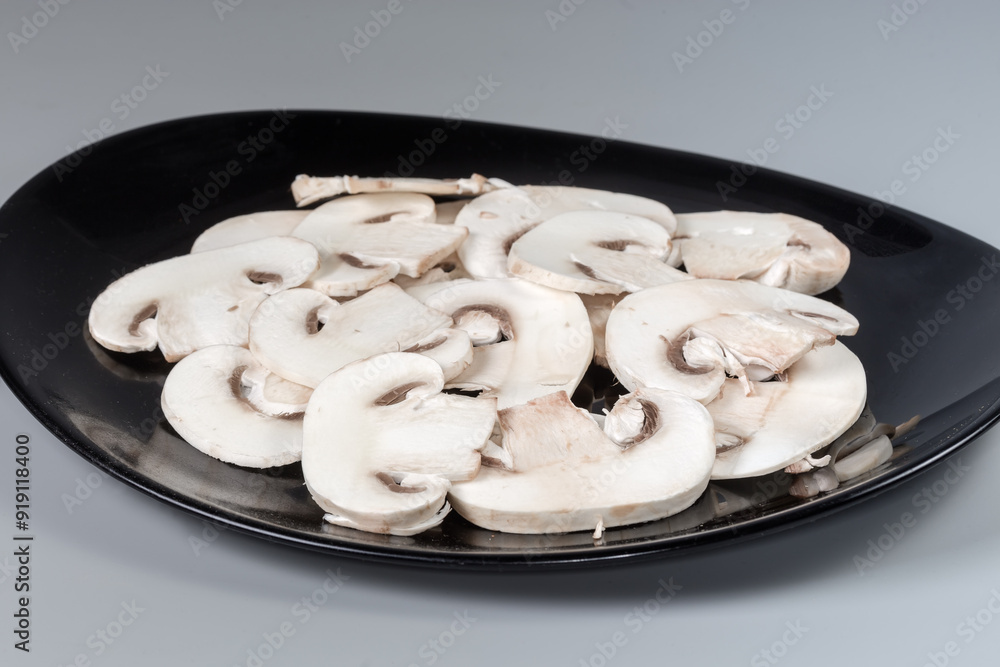 Sliced raw button mushrooms on black dish close-up Sliced raw button mushrooms on black dish close-up
