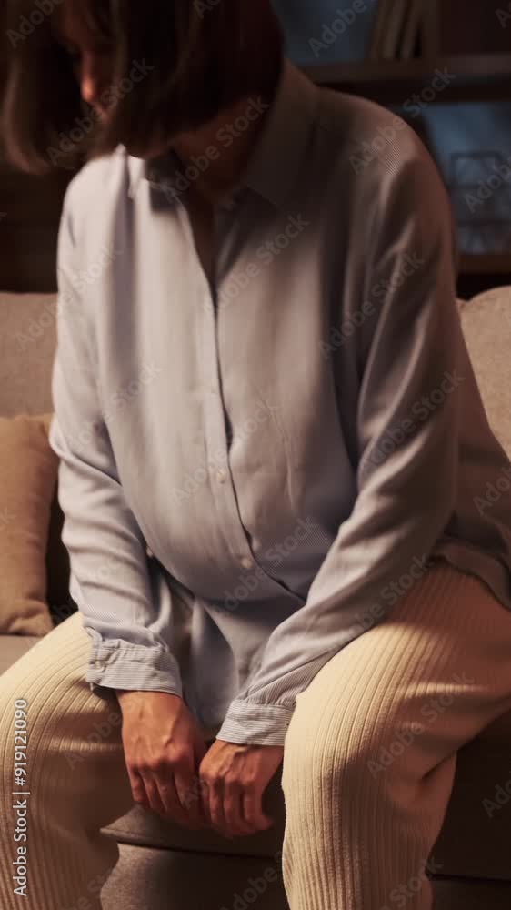 Sorrowful Caucasian middle aged woman suffering from exhaustion, emotional stress and sadness, sitting on sofa at evening home. Vertical video. Sorrowful Caucasian middle aged woman suffering from exhaustion, emotional stress and sadness, sitting on sofa at evening home. Vertical video.