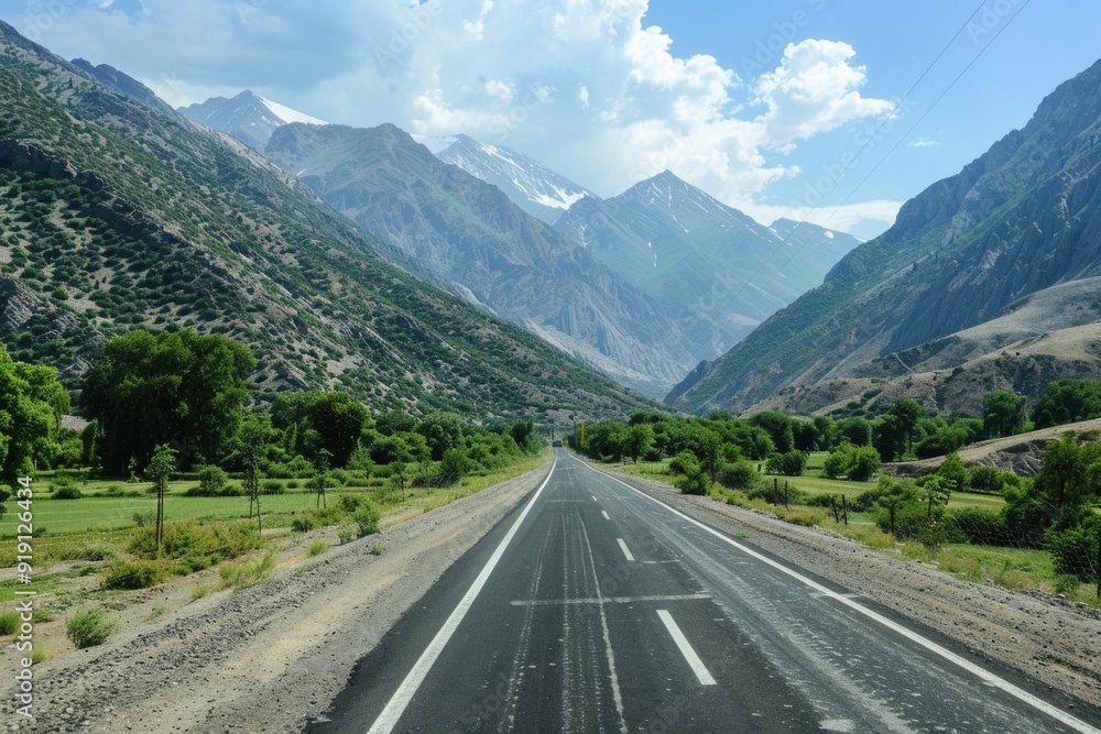 Naklejka premium A scenic view of a highway winding its way through rolling hills and towering mountains