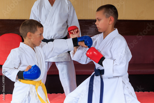 The athlete in blue pads diligently throws a straight punch at the athlete in red pads photo