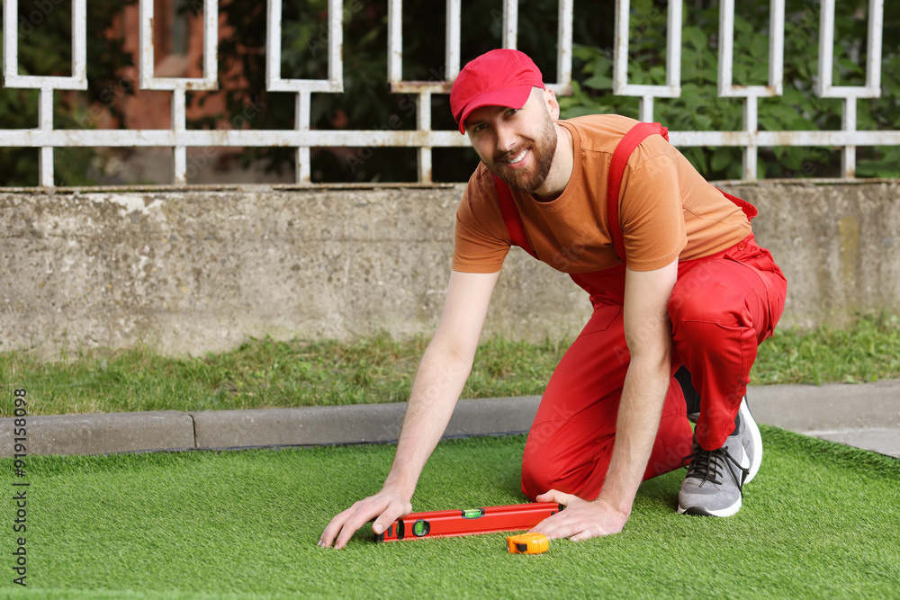 Happy young man installing artificial turf outdoors Happy young man installing artificial turf outdoors