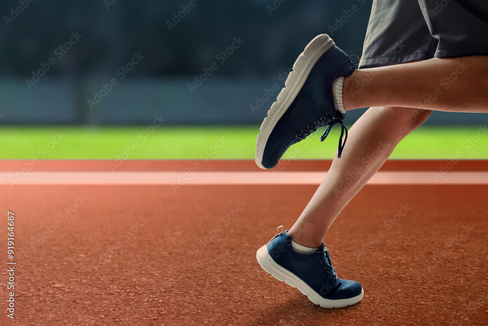 Young man runner legs sprinting in stadium field with green grass and red asphalt Young man runner legs sprinting in stadium field with green grass and red asphalt