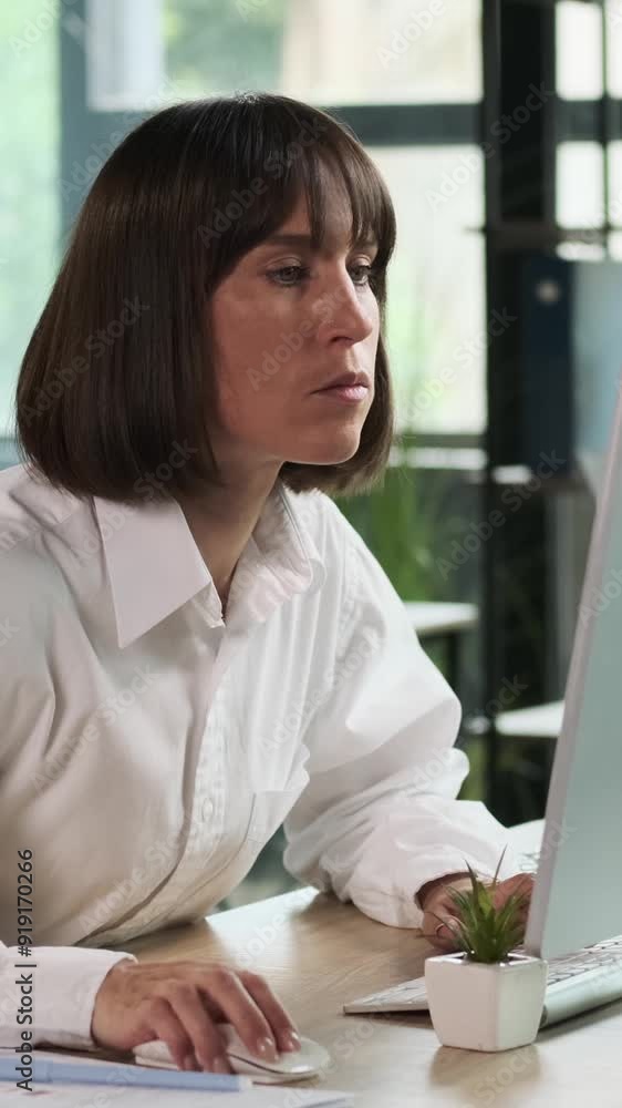 Attentive Caucasian middle aged woman thinking and using desktop computer in the office. Pensive businessperson concept. Vertical video. Attentive Caucasian middle aged woman thinking and using desktop computer in the office. Pensive businessperson concept. Vertical video.