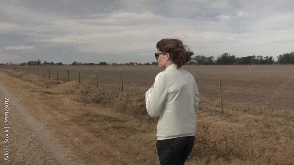 Slow motion, wide view of a young adult female walking with her pet dog in a rural road.