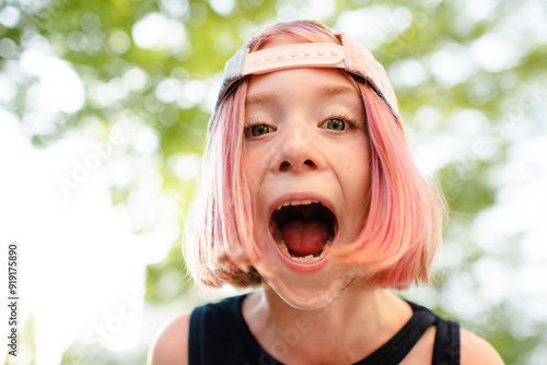Stylish kid girl with blonde pink hairstyle pre teen age 9 -10 year old with open mouth wearing cap outdoor. Childhood
