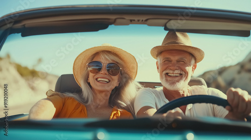 A joyful senior couple during a road trip. They are happily seated in their car, with a picturesque view of the open road and countryside behind them