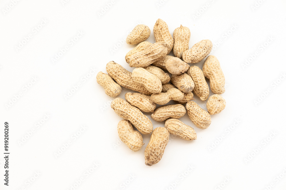 A small pile of peanuts in their shells, scattered on a white surface. A simple and natural snack. A small pile of peanuts in their shells, scattered on a white surface. A simple and natural snack.