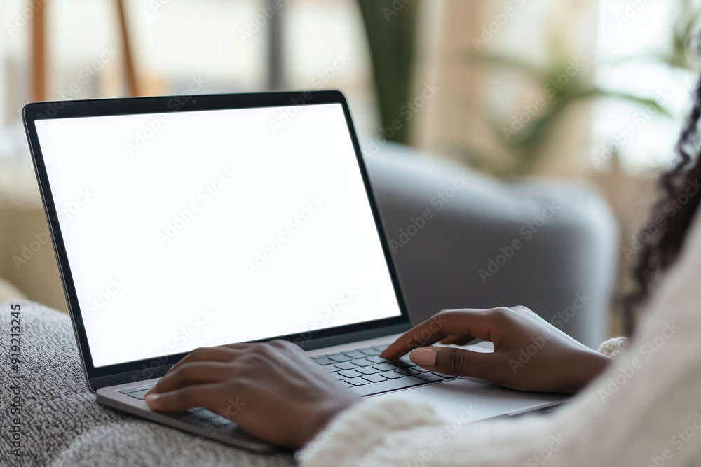 Close-up of a person typing on a laptop with a blank white screen, seated in a comfortable, home-like setting.
Close-up of a person typing on a laptop with a blank white screen, seated in a comfortable, home-like setting.