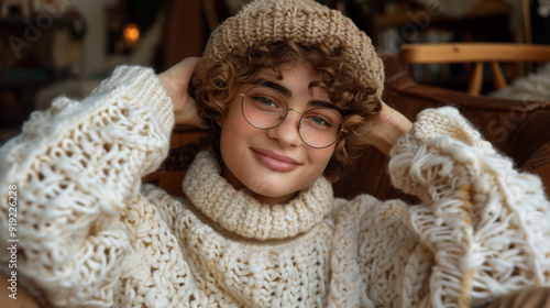 A happy young woman wearing glasses and cozy knitwear, smiling warmly indoors. Trendy voluminous knitted sweater in the fashion trends of winter 2024-2025. photo