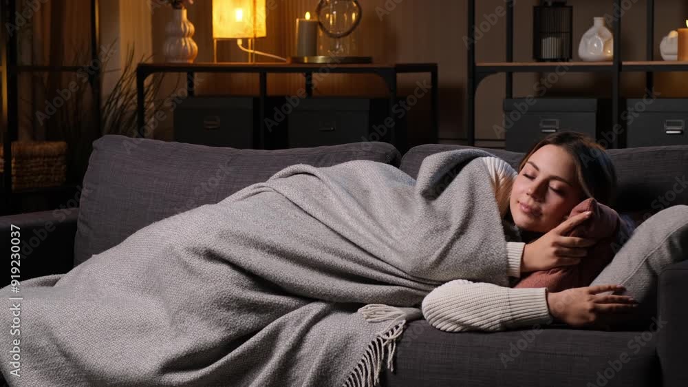 Smiling Caucasian young woman sleeping on sofa, wrapped on blanket at evening home. Relaxation, resting. Exhaustion and recreational dreaming. Smiling Caucasian young woman sleeping on sofa, wrapped on blanket at evening home. Relaxation, resting. Exhaustion and recreational dreaming.