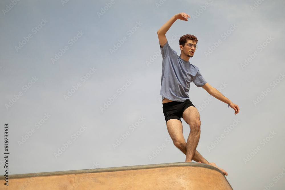 Fototapeta premium Ballet dancer in blue shirt gracefully balances under a clear sky.