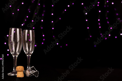 Champagne glasses, cork, and bottle arranged on the left side with a black background and purple out-of-focus lights, ideal for holiday and party themes. photo