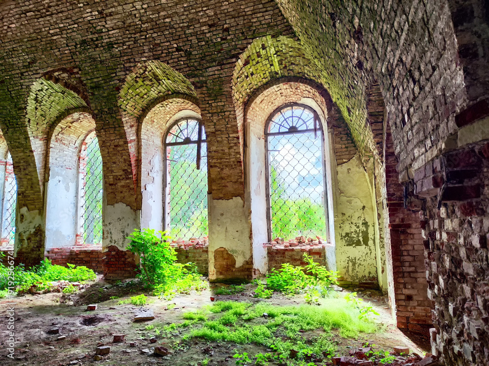 Fototapeta premium Light filters through arched windows illuminating the overgrown interior of an abandoned brick structure