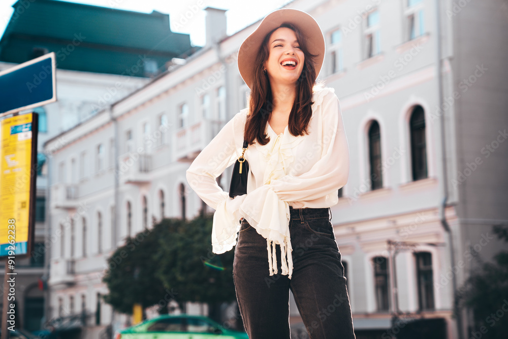 Portrait of young beautiful smiling hipster woman in trendy summer white blouse and jeans. Carefree woman posing in the street in sunny day. Positive model outdoors. Cheerful and happy Portrait of young beautiful smiling hipster woman in trendy summer white blouse and jeans. Carefree woman posing in the street in sunny day. Positive model outdoors. Cheerful and happy