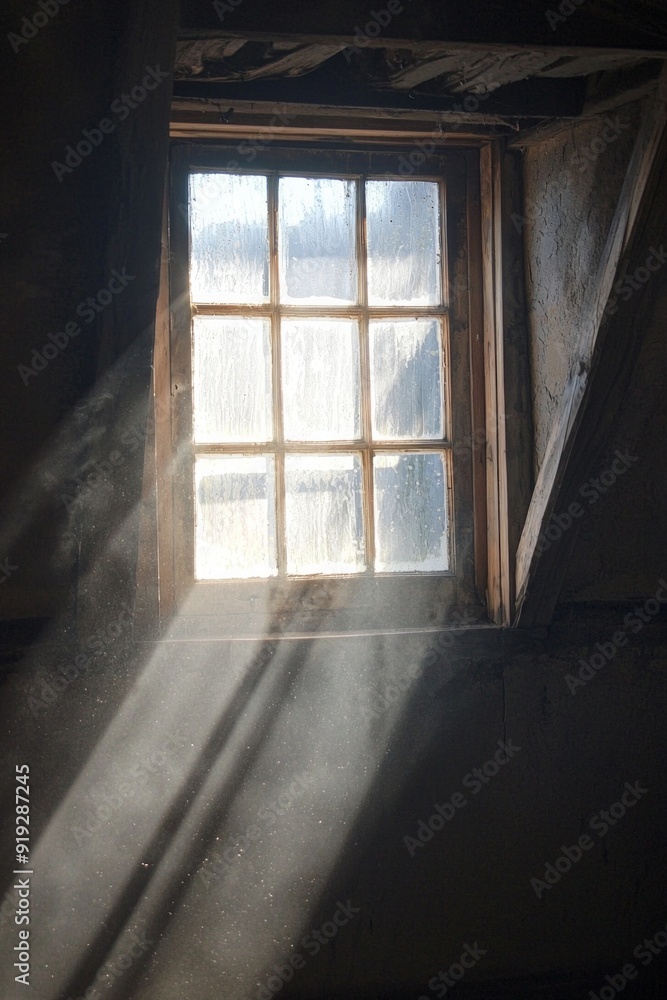 A window in a dimly lit attic, with a single beam of sunlight piercing through the dusty glass. 
