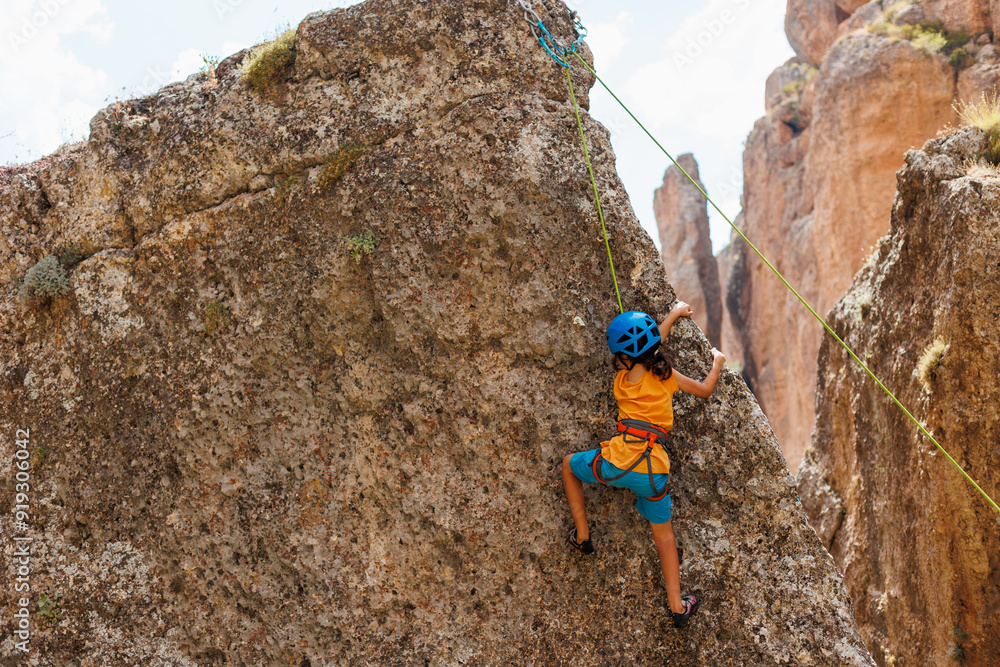 Obraz premium sport in summer camp. a child is rock climbing at a summer camp. rock climber boy. sport in nature on a sunny day. cute teenager climbs a rock with a belay. summer rest.